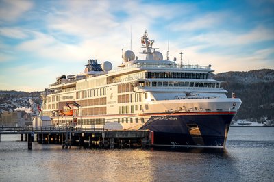 Das Traumschiff Hanseatic nature liegt im Hafen. Die Sonne scheint und im Hintergrund sind Berge zu sehen.