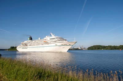 Ein weißes Kreutzfahrtschiff fährt auf den Nord-Ostsee-Kanal entlang. Der Himmel ist blau.